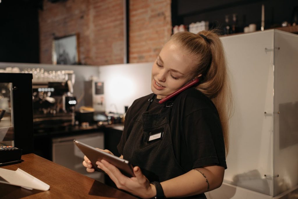 pexels-photo-6612691 Young woman in café multitasks with a tablet and phone at the counter.